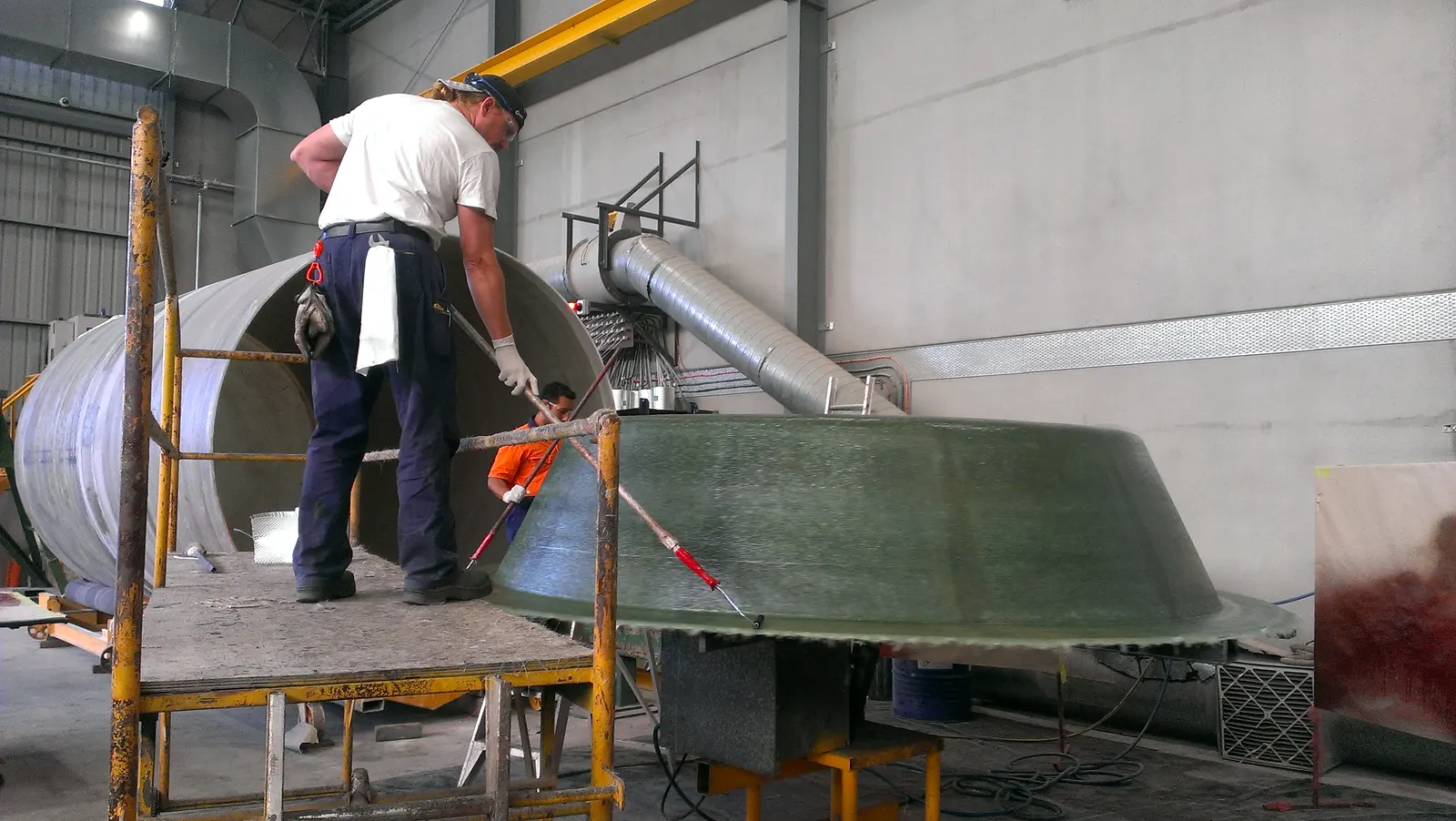 Laminator trimming the flange of a fibreglass tank end on a work platform in the factory
