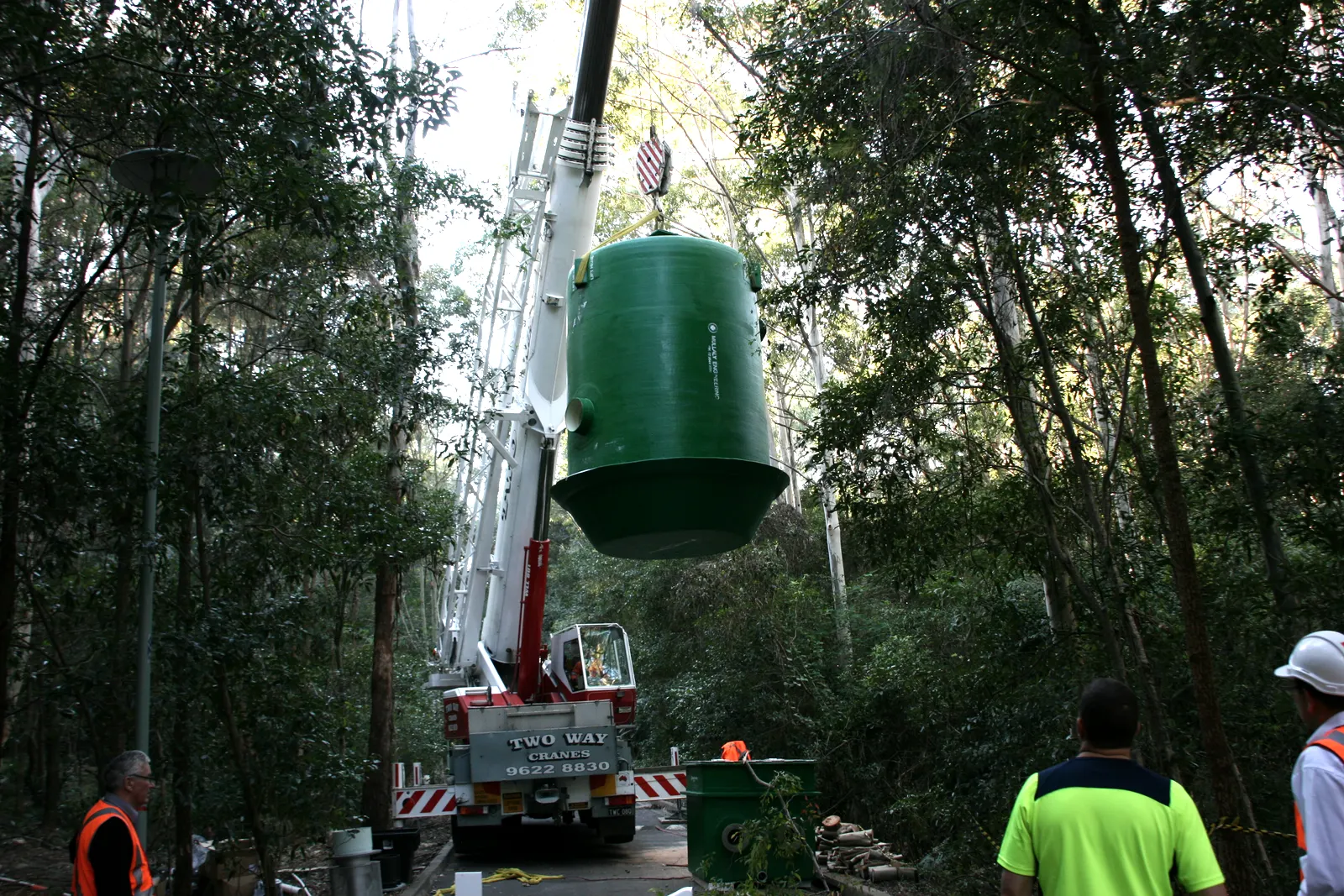 Crane lifting a Mullaly FRP wet well between gum trees with the install crew watching, Triple M IBM project