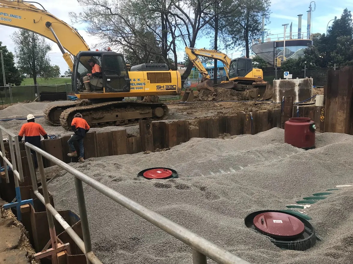 Excavators backfilling over buried fibreglass water storage tanks at Gympie, with only the access risers left showing
